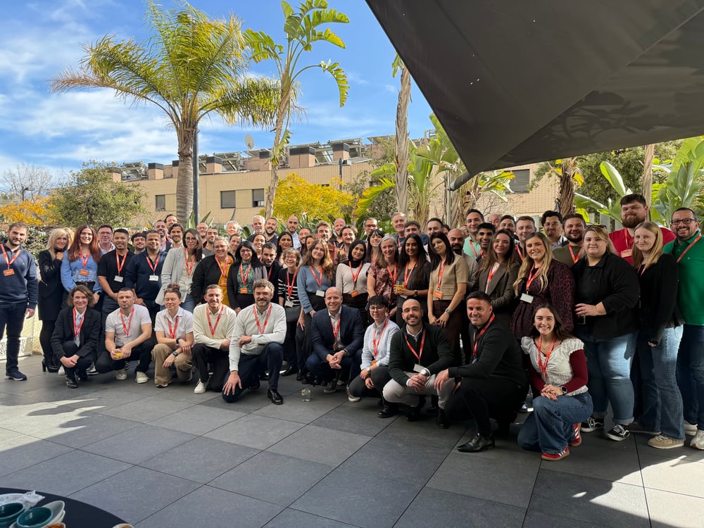 A group of employees outside at an event in Barcelona, with blue skies and palm trees in the background.