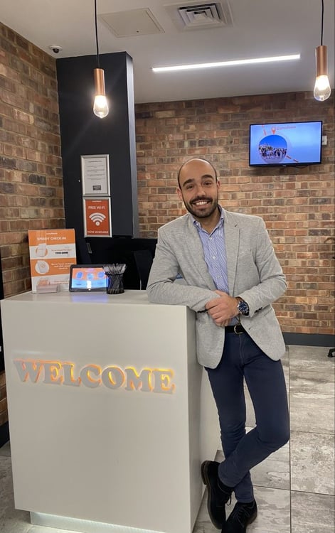 Smiling manager Alvaro at the illuminated 'WELCOME' reception desk in the modern easyHotel Barcelona lobby, featuring self-check-in and free Wi-Fi signage.