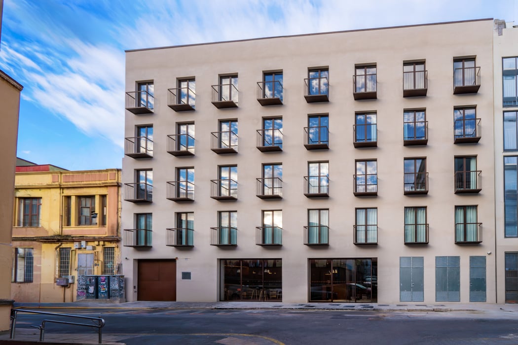 EasyHotel Valencia Ciutat Vella exterior: A multi-story beige building with numerous small windows and balconies, under a partly cloudy blue sky.