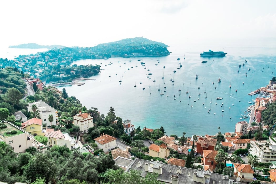 Panoramic view of the vibrant Bay of Villefranche-sur-Mer on the French Riviera, showcasing countless boats, a large cruise ship, and colorful coastal homes nestled on the lush green hills.