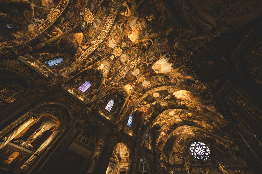 Ornate Baroque ceiling and intricate frescoes of Valencia Cathedral in Spain, featuring golden stucco details, arched architecture, and stained glass windows.