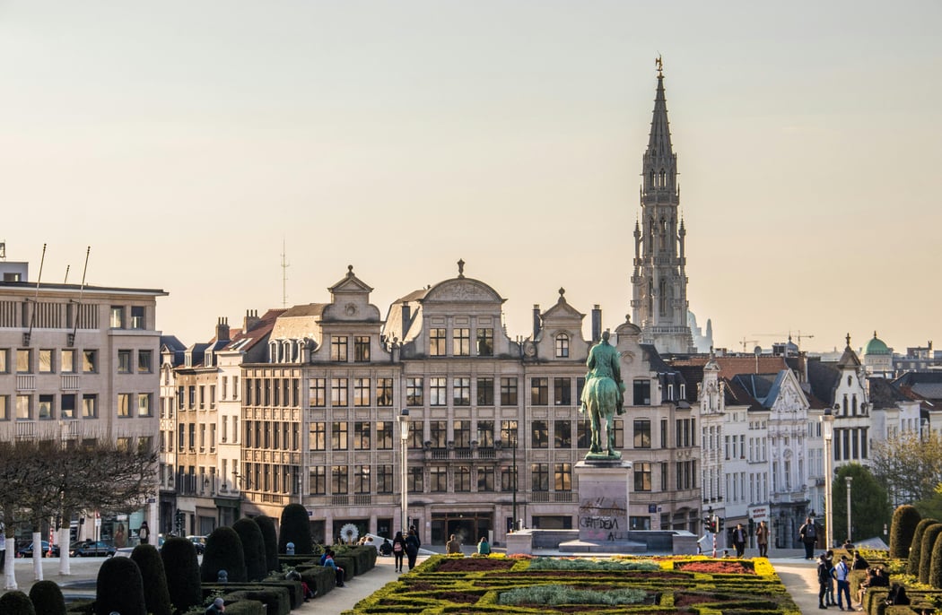 Brussels cityscape from Mont des Arts, featuring the King Albert I equestrian statue, formal gardens, historic buildings, and the Gothic spire of Brussels Town Hall against a clear sky.