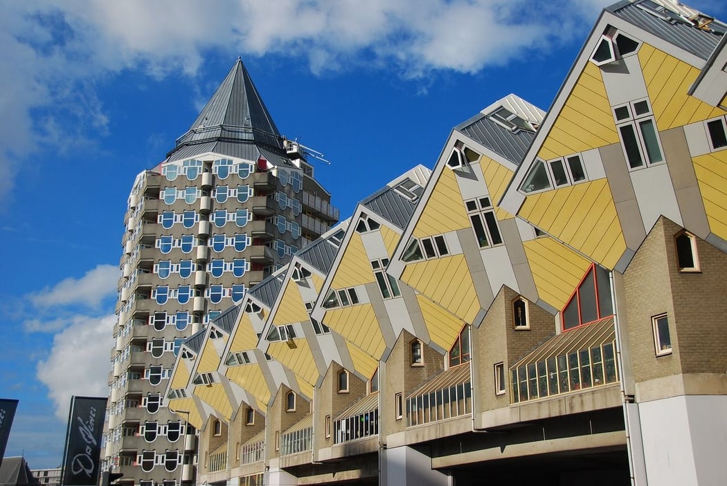 Iconic yellow Cube Houses and the tall Pencil House building under a blue sky in Rotterdam, Netherlands.