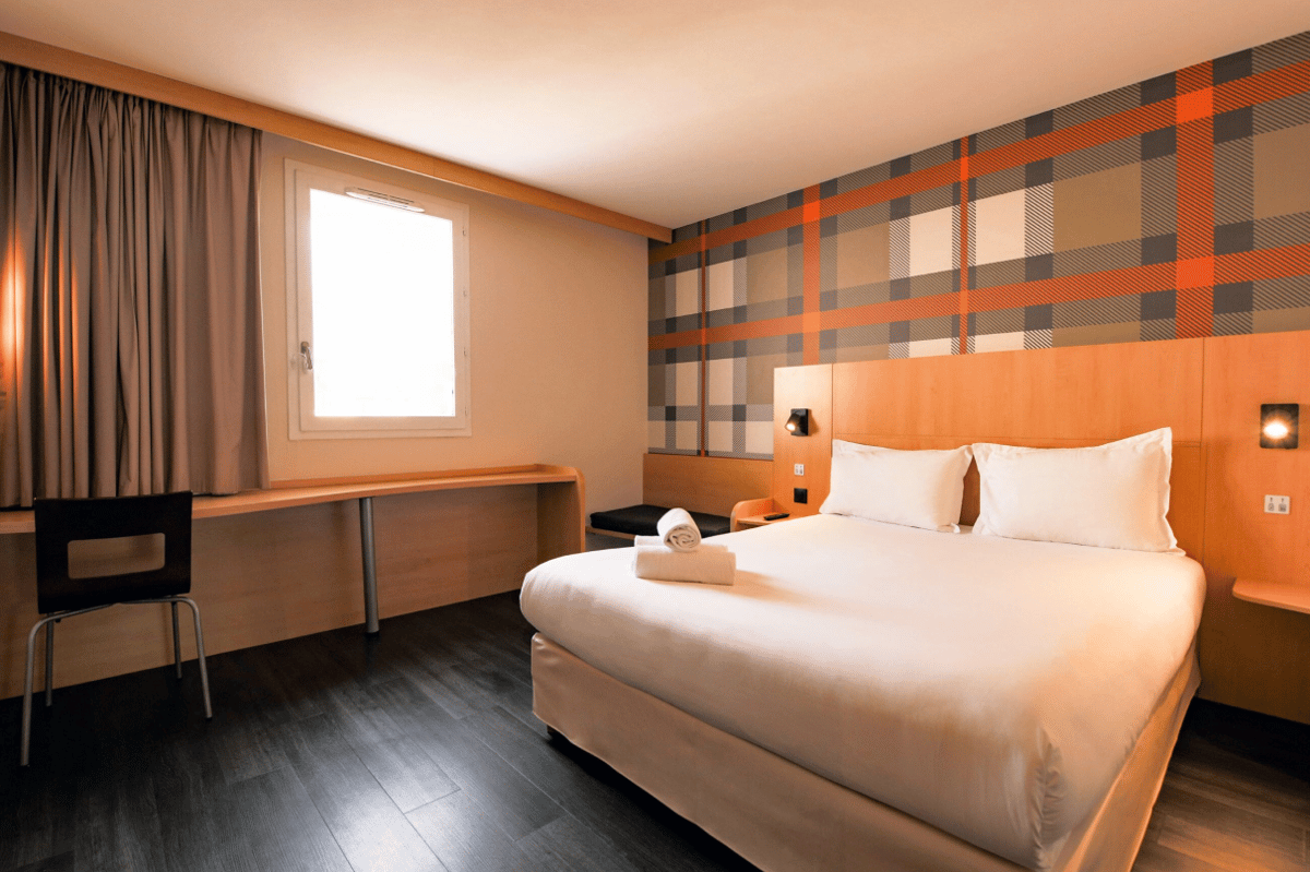 easyHotel Nice Palais des Congres hotel room with double bed, orange and grey plaid feature wall, and desk area.
