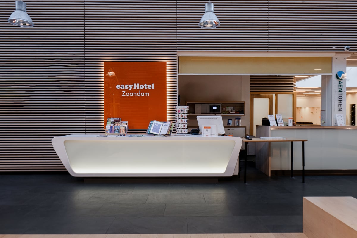 Modern easyHotel Zaandam reception desk with orange logo sign on a striped wall, showcasing the hotel lobby.
