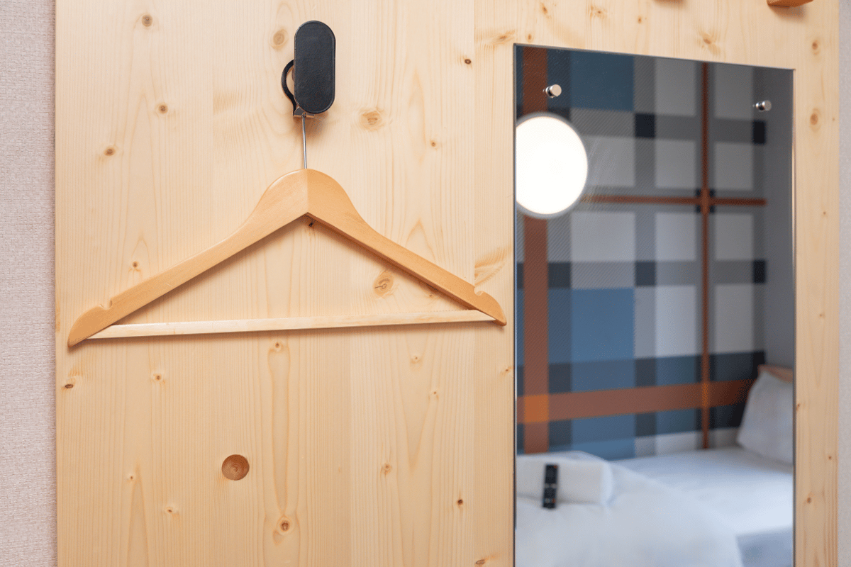 ALT: easyHotel Glasgow room interior with a light wood panel, wooden hanger, and a mirror reflecting the bed and signature plaid wall design.