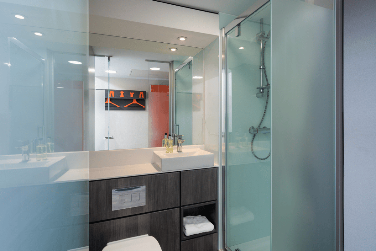 Modern easyHotel Ipswich bathroom with white rectangular sink, dark wood vanity, and clear glass shower enclosure.