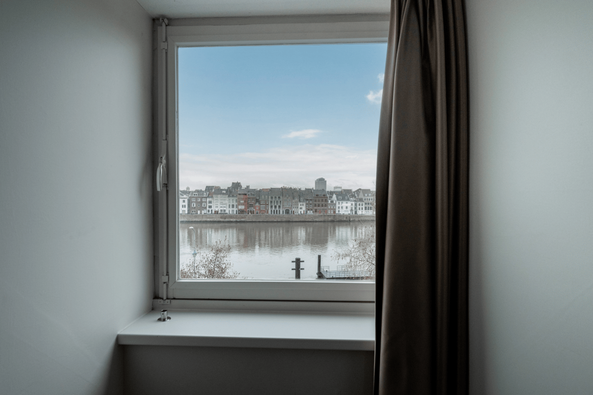 A view from an easyHotel Maastricht room window, showcasing the Meuse river and the historic city buildings on the opposite bank under a clear blue sky.