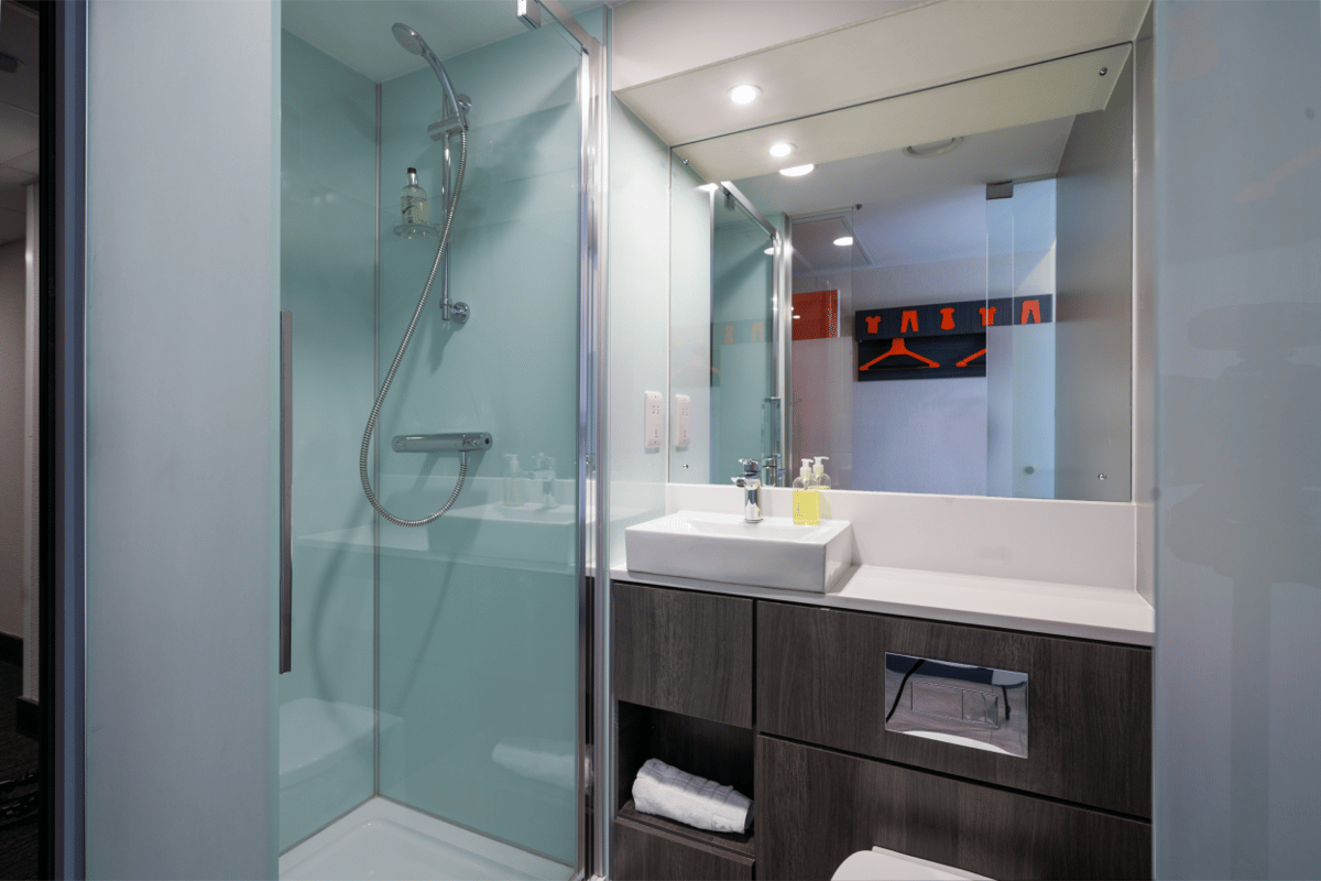 Modern bathroom in an easyHotel Sheffield room, featuring a turquoise-walled shower, square basin sink, and a mirror reflecting the room's distinctive orange clothes hangers.