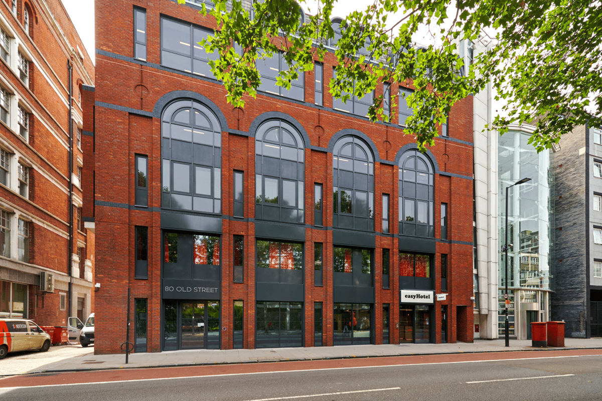 Exterior view of the easyHotel London City Shoreditch building on Old Street, featuring its modern red brick facade, large arched windows, and visible easyHotel signage at street level.
