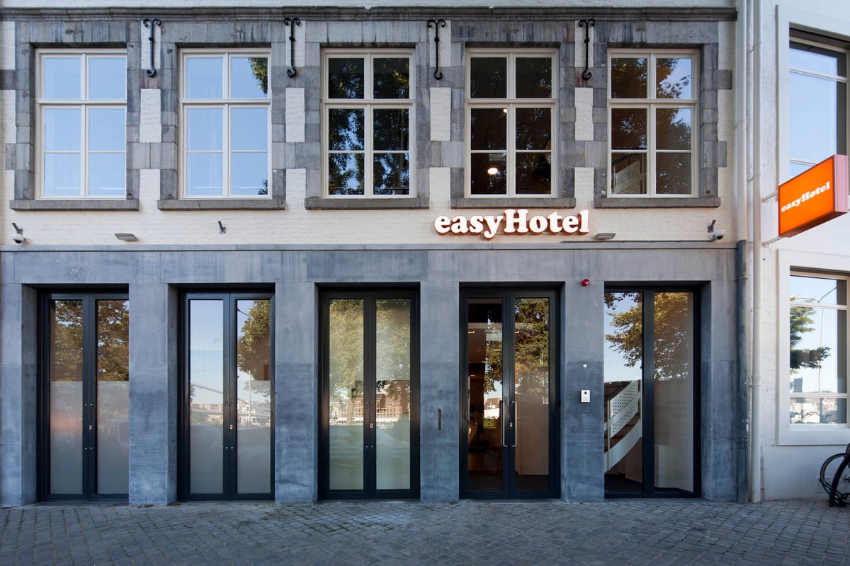 easyHotel Maastricht exterior, featuring a historic stone and white brick facade, the prominent easyHotel logo, and multiple glass entrances from a cobblestone street.