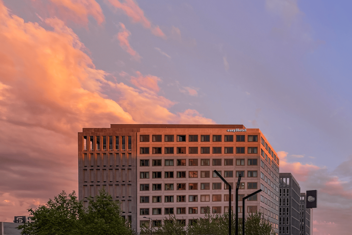 Exterior view of the easyHotel Paris Nord Aubervilliers building facade at sunset, featuring a modern multi-story design with many windows, illuminated by the warm glow of the setting sun and dramatic orange and pink clouds.