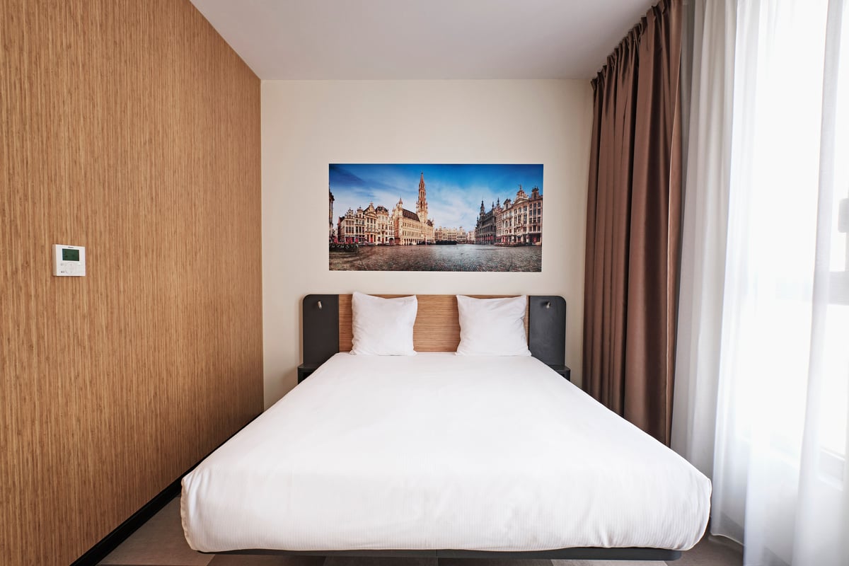 easyHotel Brussels City Centre hotel room featuring a double bed, white bedding, and a panoramic wall mural of the Grand Place in Brussels.