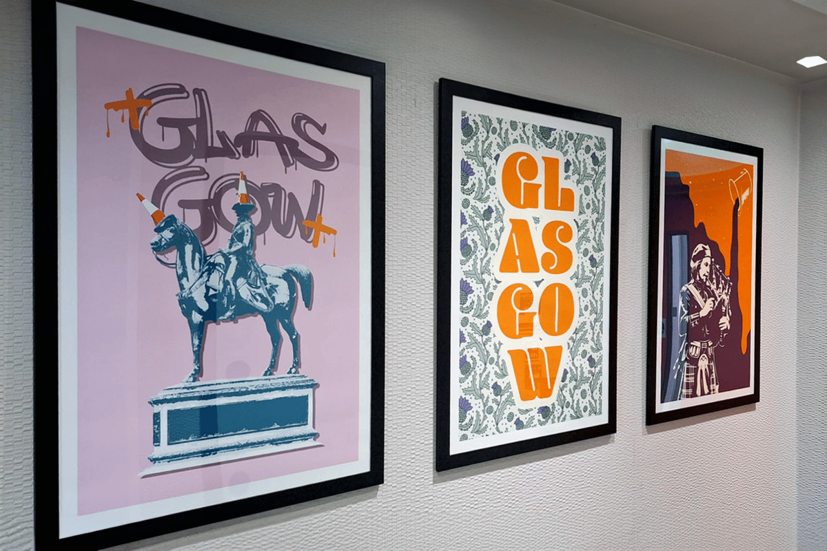 Glasgow-themed artwork displayed in an easyHotel room, featuring framed prints of the Duke of Wellington statue with a traffic cone, a 'GLASGOW' text design with thistles, and a bagpiper.