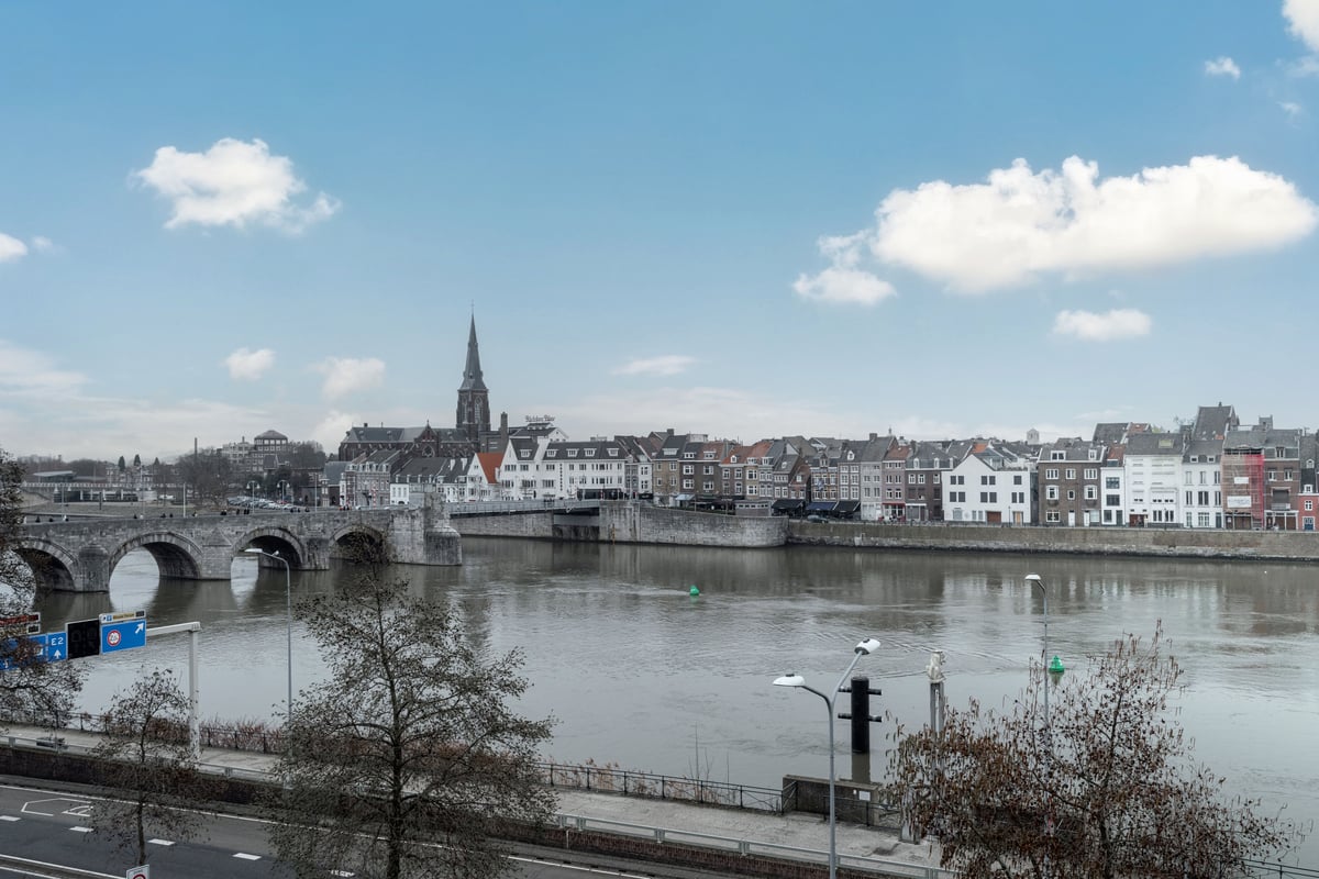 Scenic view of Maastricht from easyHotel, showcasing the Maas River, the historic Sint Servaasbrug stone bridge, the iconic Onze Lieve Vrouwekerk church spire, and a row of traditional buildings lining the riverbank under a partly cloudy sky.