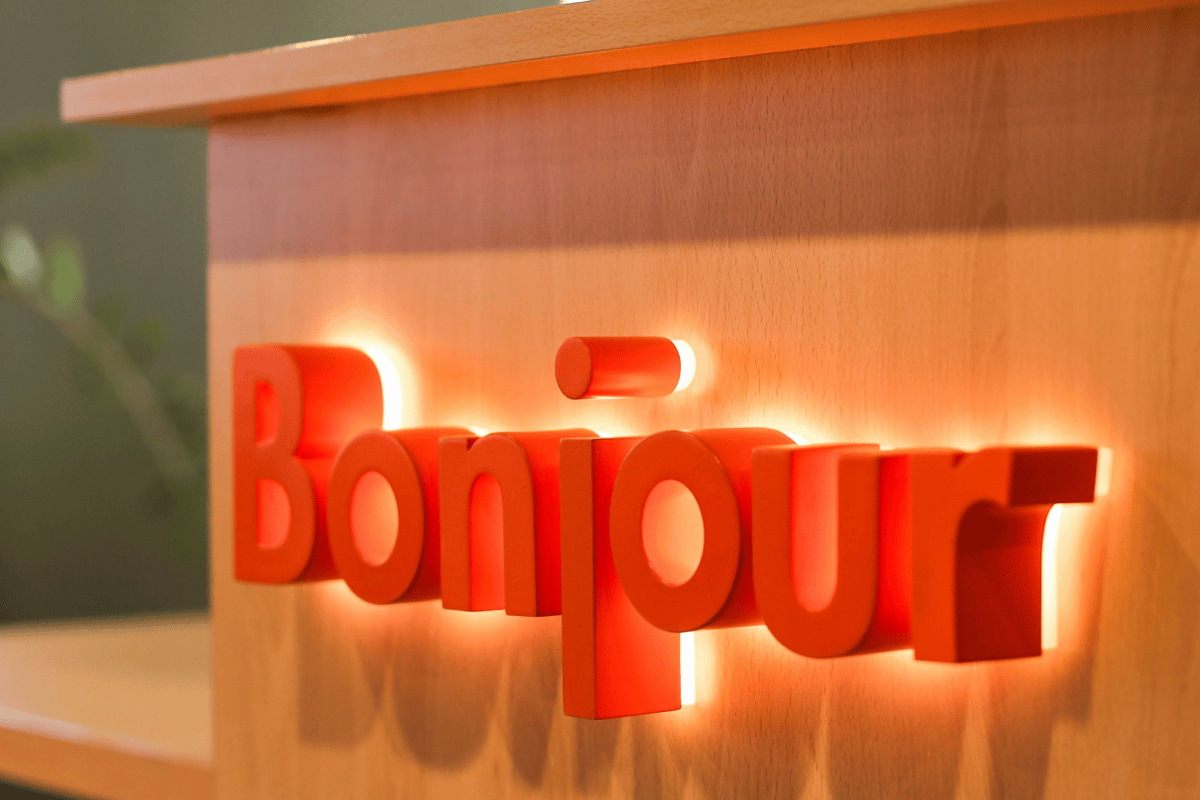 Bright orange 'Bonjour' welcome sign with backlighting on a light wood wall at easyHotel Nice Palais des Congres.