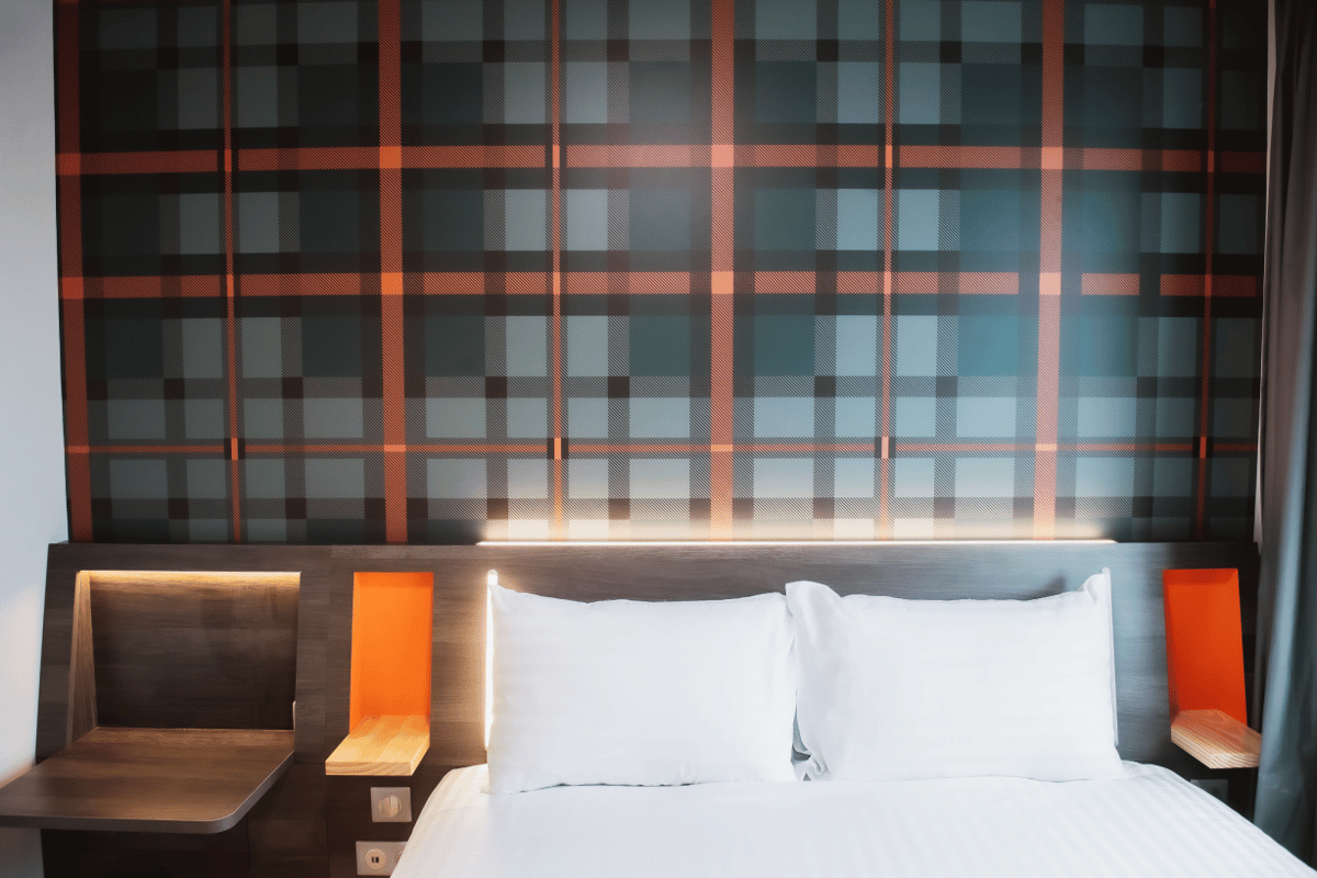 EasyHotel Paris Nord Aubervilliers room featuring a neatly made bed with white linens, a dark wooden headboard with warm integrated lighting, and a unique dark green and orange plaid patterned wall.