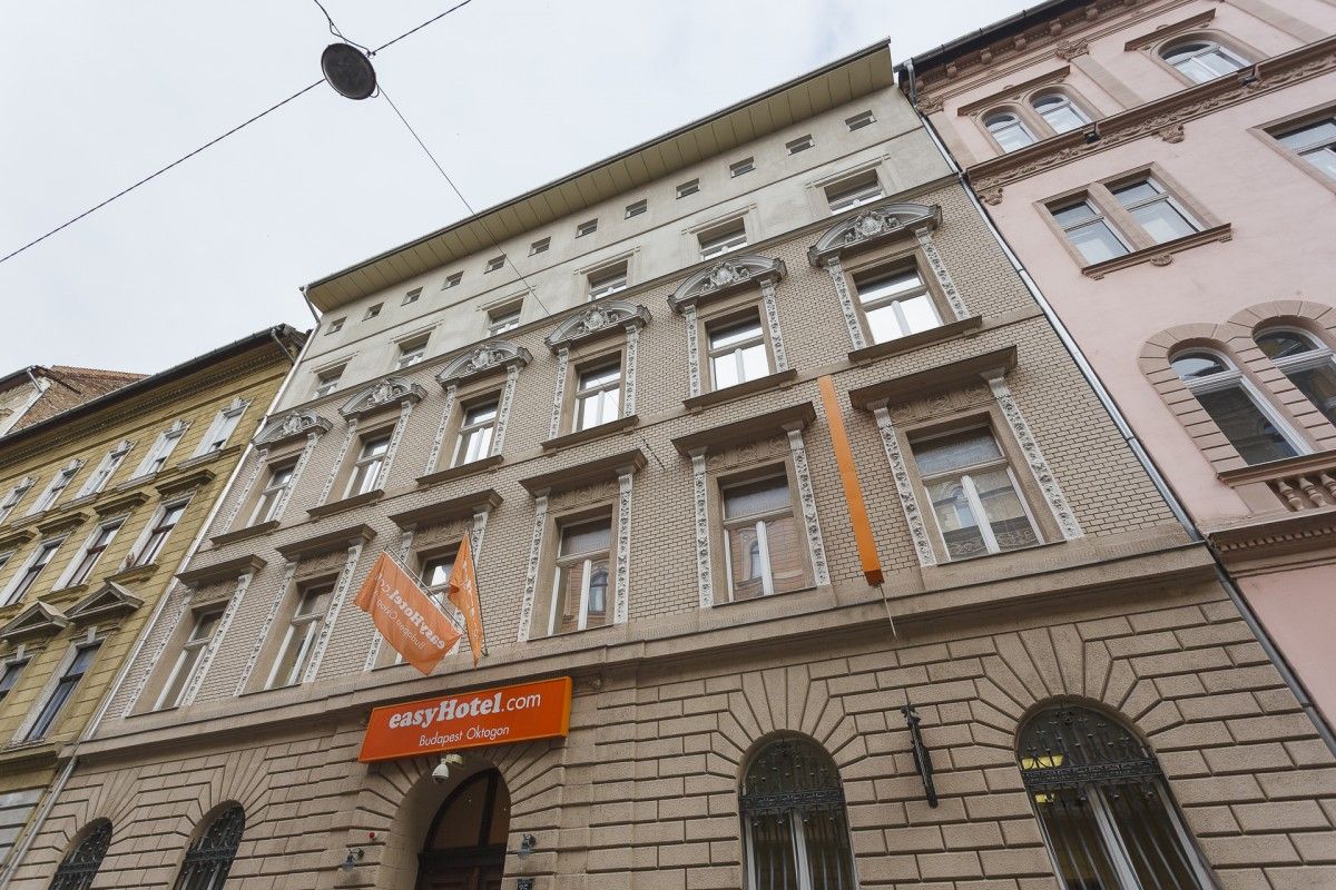 Exterior facade of easyHotel Budapest Oktogon, a multi-story light brick building with ornate window details and orange easyHotel signage, on a city street.