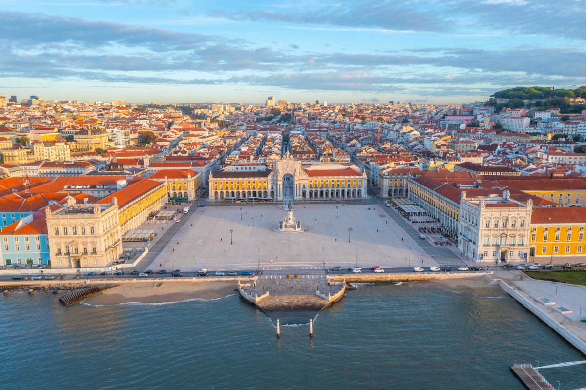 Large waterfront square with central statue, surrounded by colorful buildings.