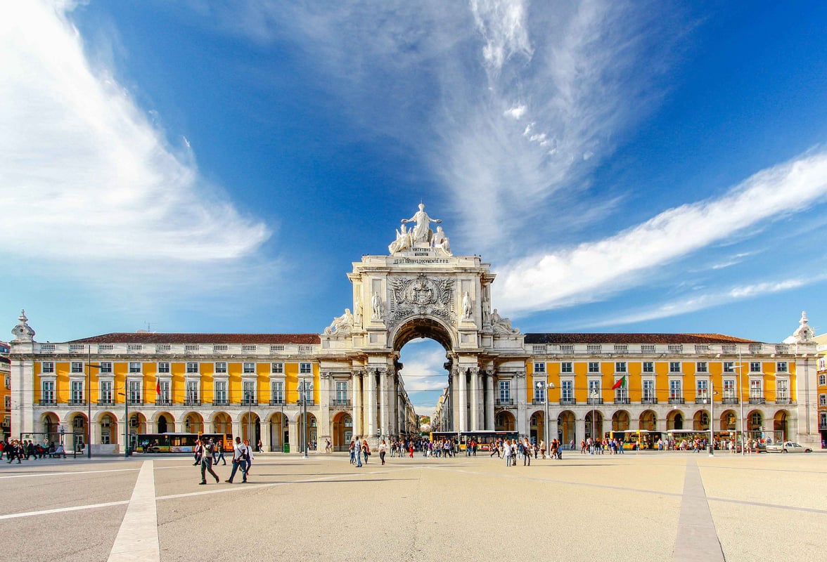 easyHotel Lisbon. Grand stone arch with statues, yellow buildings, and people in plaza.