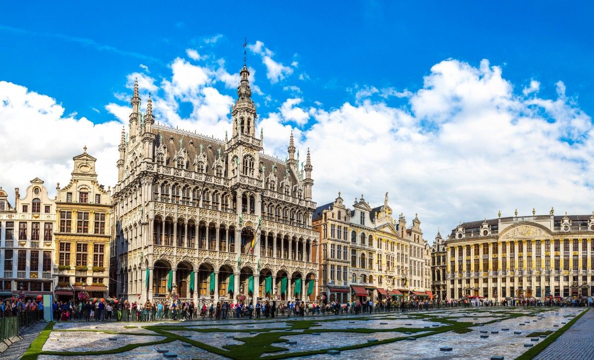 Grand Place in Brussels, Belgium, featuring the magnificent Gothic Town Hall and ornate Baroque guildhalls surrounding the historic square under a bright blue sky.