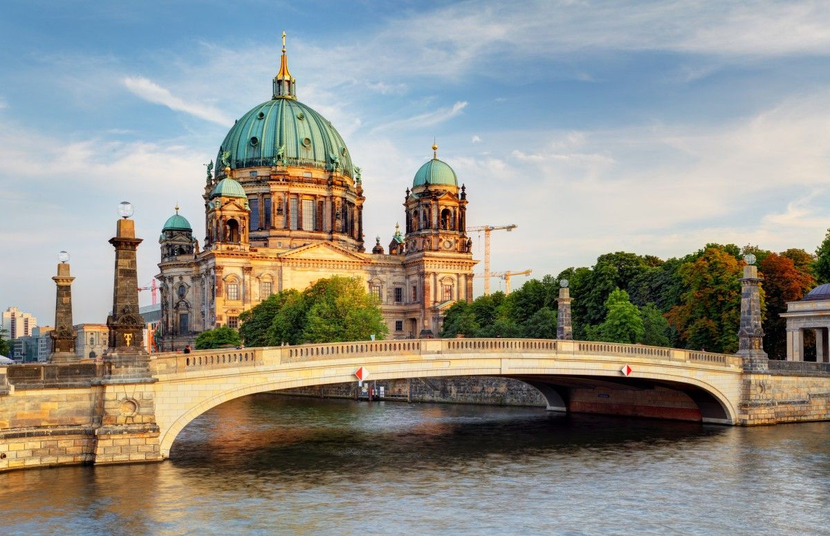 Berlin Cathedral (Berliner Dom) and Schlossbrücke bridge over the Spree River in Berlin, Germany, under a bright blue sky.