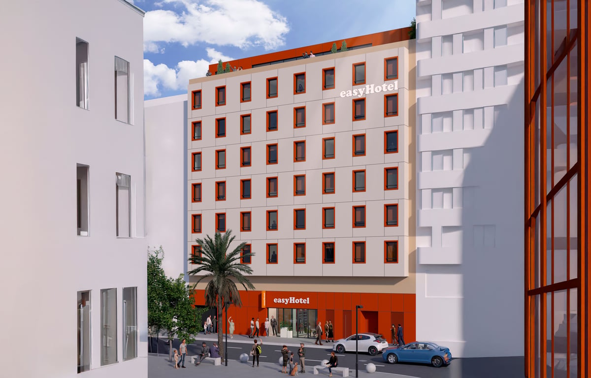 Modern orange and white building with multiple windows, featuring the "easyHotel" logo, located on a city street with pedestrians.