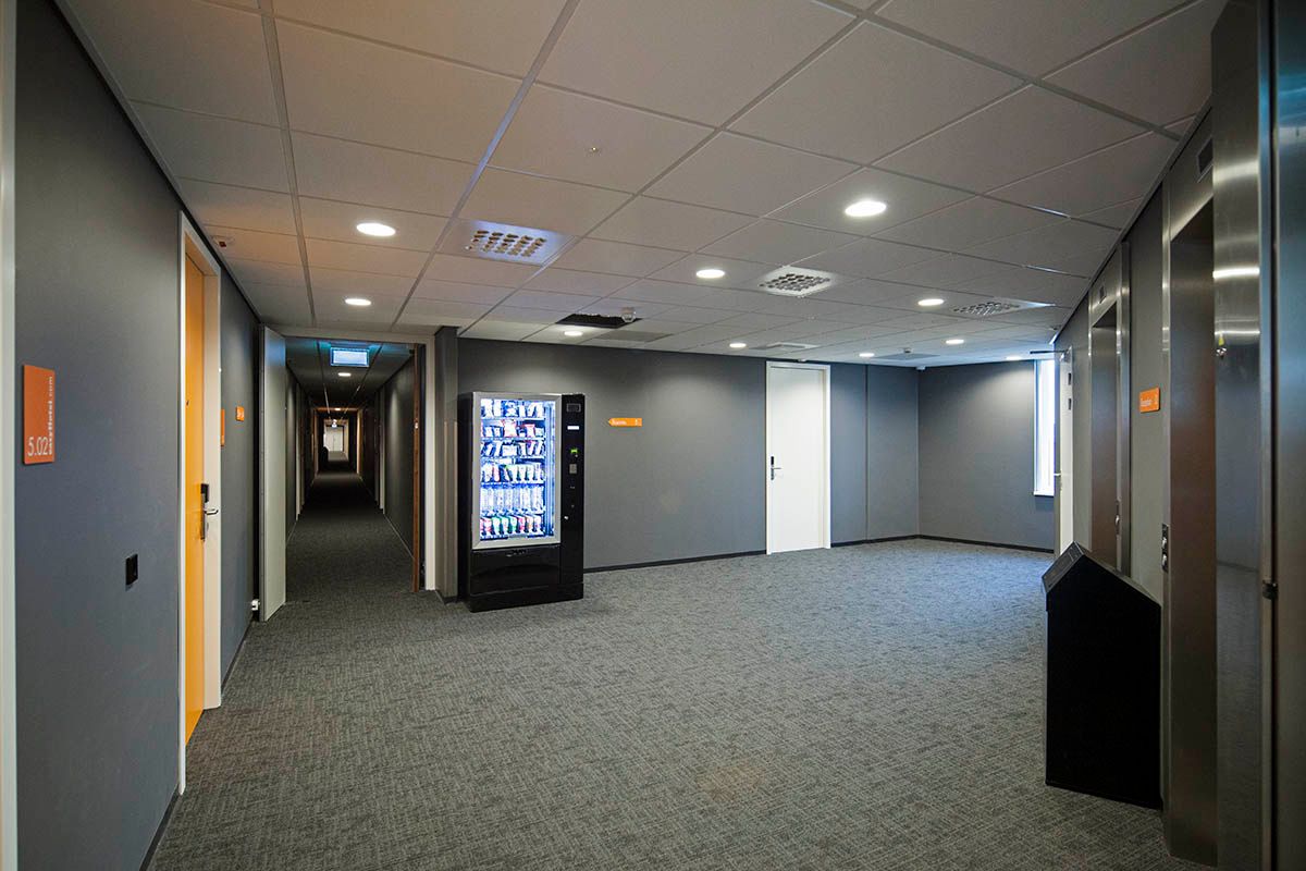 Modern easyHotel Amsterdam Arena corridor featuring a vending machine, guest room doors, and elevators.