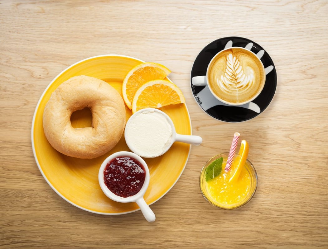 EasyHotel Amsterdam Zaandam breakfast: bagel, jam, yogurt, orange slices, and a latte with a smoothie on a wooden table.