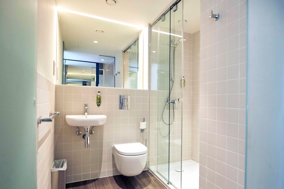 EasyHotel Barcelona Fira double bathroom with white sink, toilet, and walk-in shower featuring glass screen and light beige tiles.