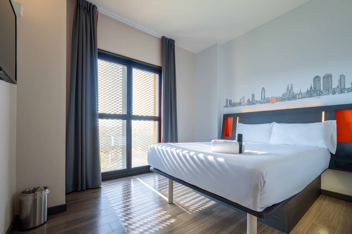 EasyHotel Barcelona Fira double room with a double bed, white linens, and city skyline wall art.