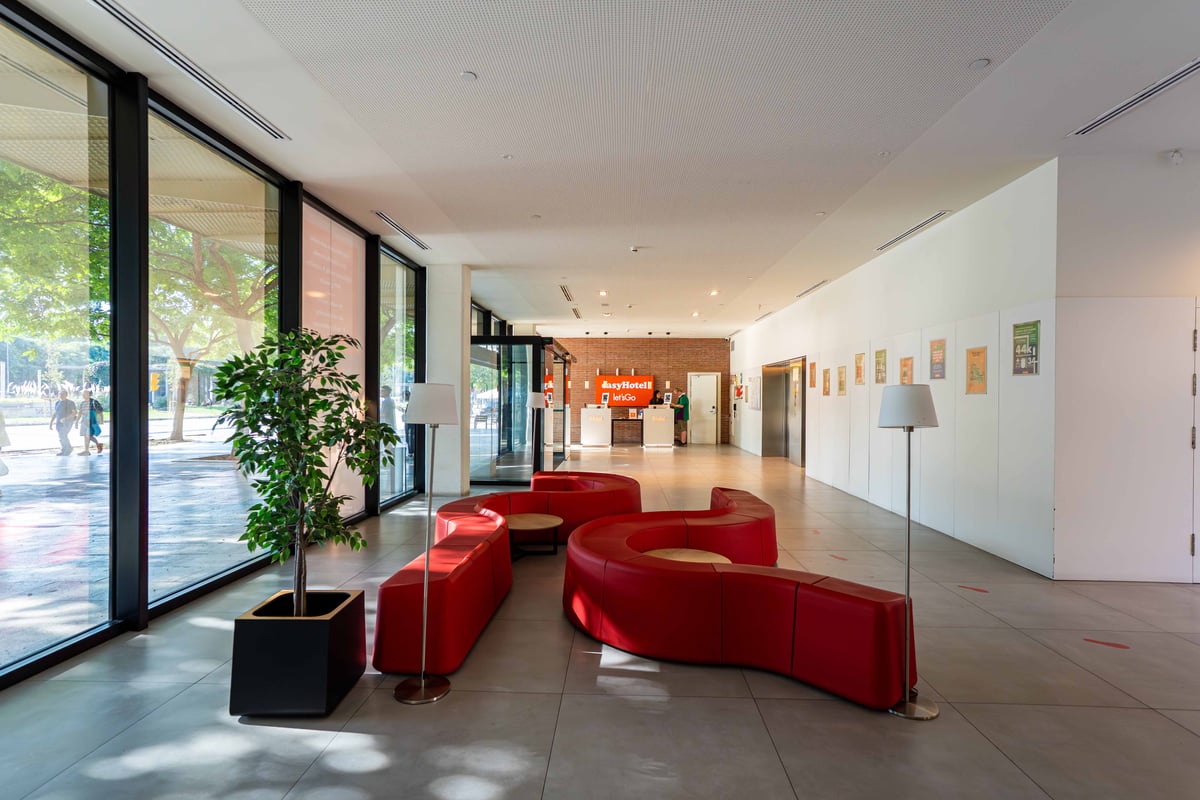 EasyHotel Barcelona Fira reception area with red seating, large windows, and minimalist decor.