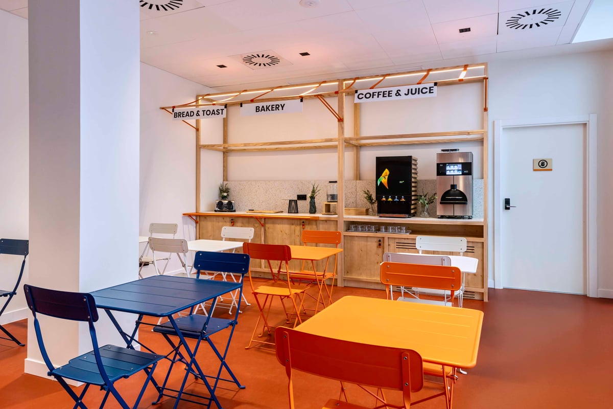 EasyHotel Barcelona La Sagrera breakfast room with colorful tables and chairs, coffee and juice station, and bakery items.