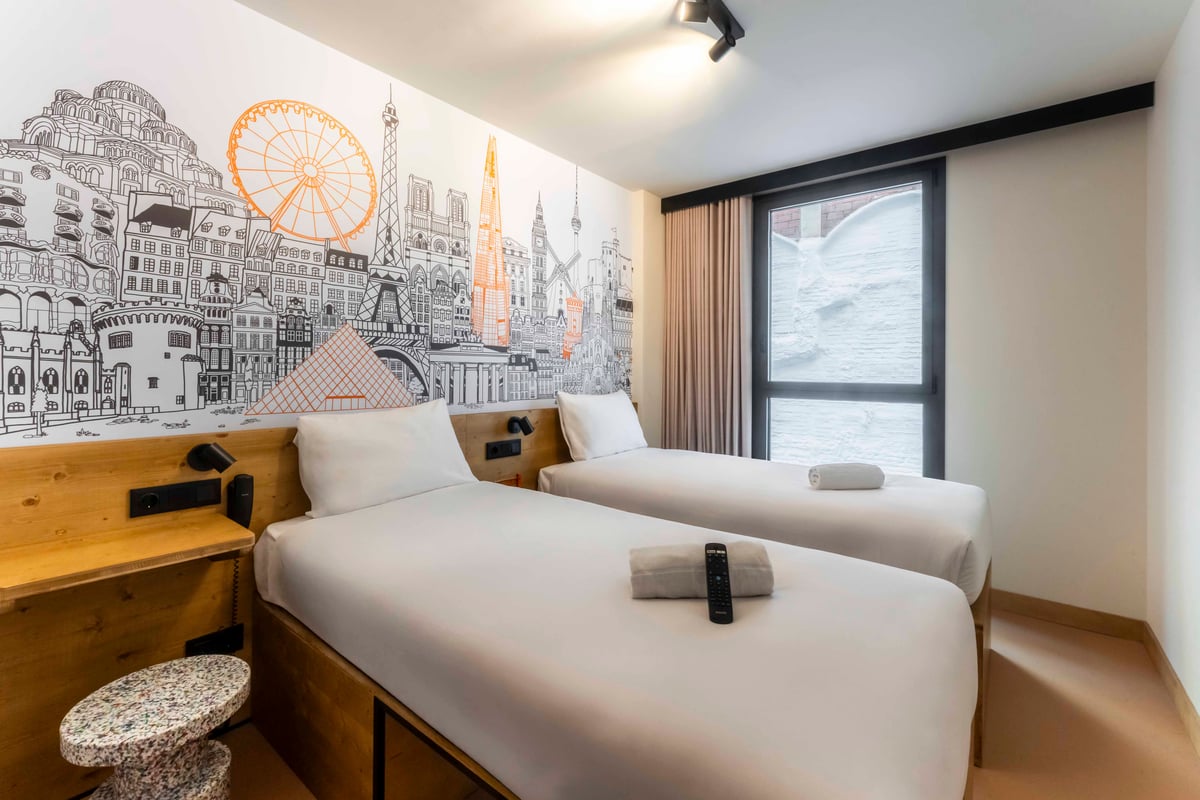 EasyHotel Barcelona La Sagrera twin room with two single beds, white linens, and a city-themed wallpaper.