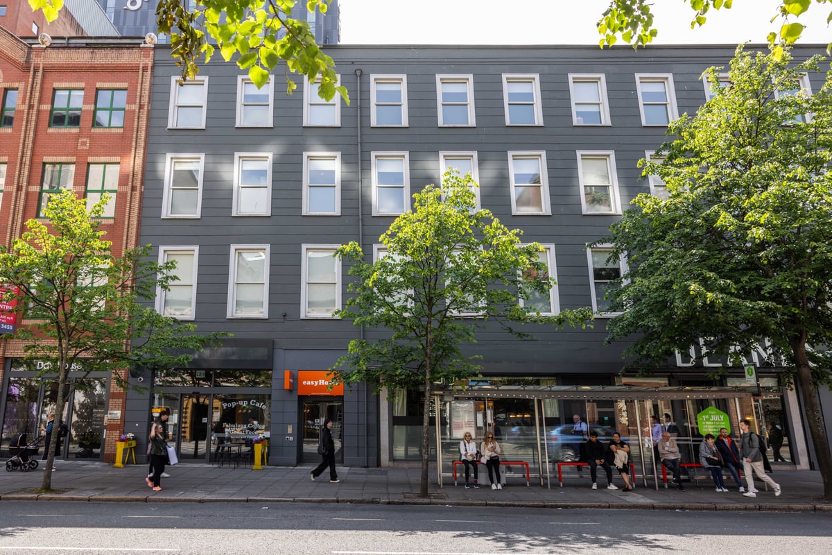 easyHotel Belfast exterior showing a grey multi-story building with white-framed windows and an orange easyHotel sign above the entrance at street level.
