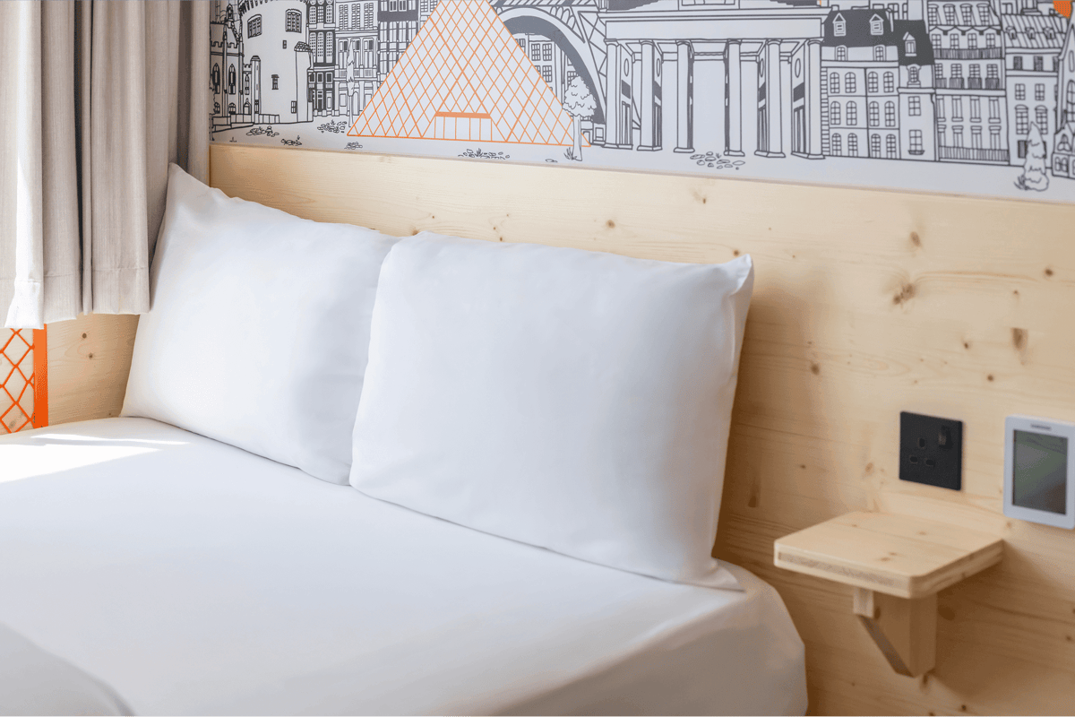EasyHotel Croydon double room with white bedding and pillows against a light wood headboard featuring a cityscape mural.