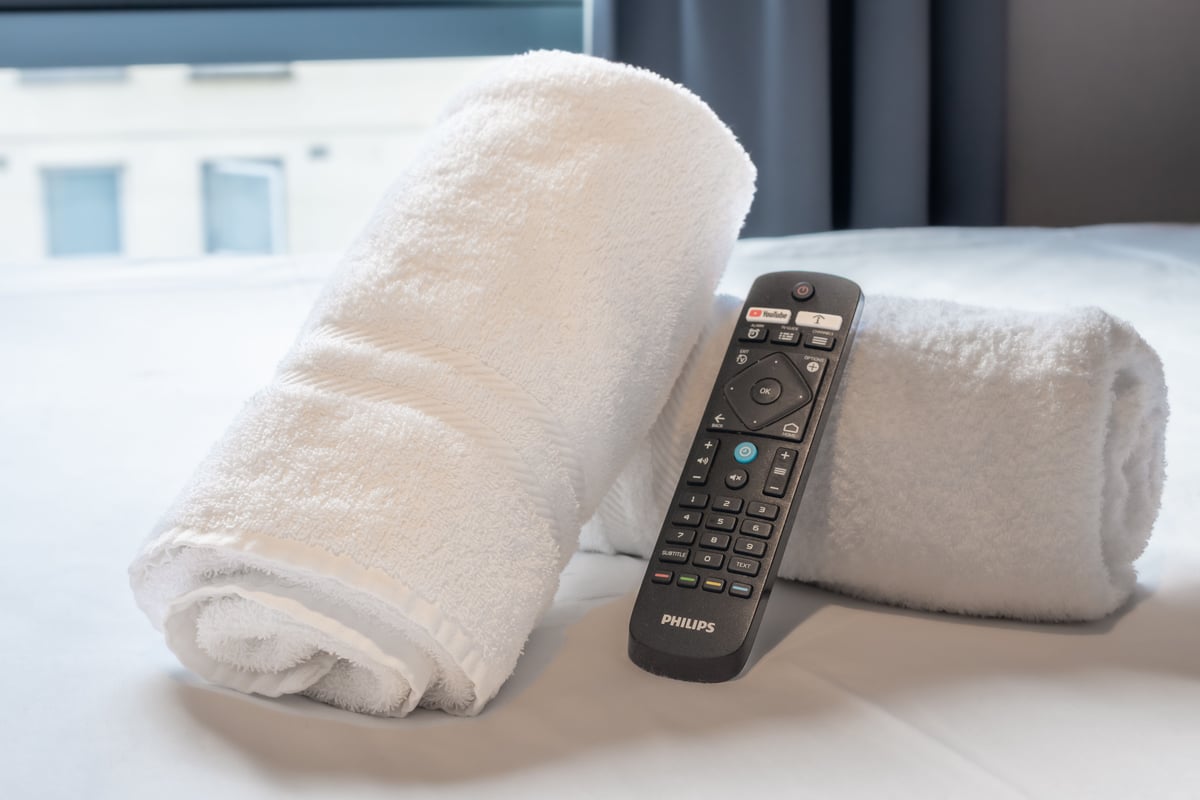 Two white bath towels and a remote control for a TV on a double bed.