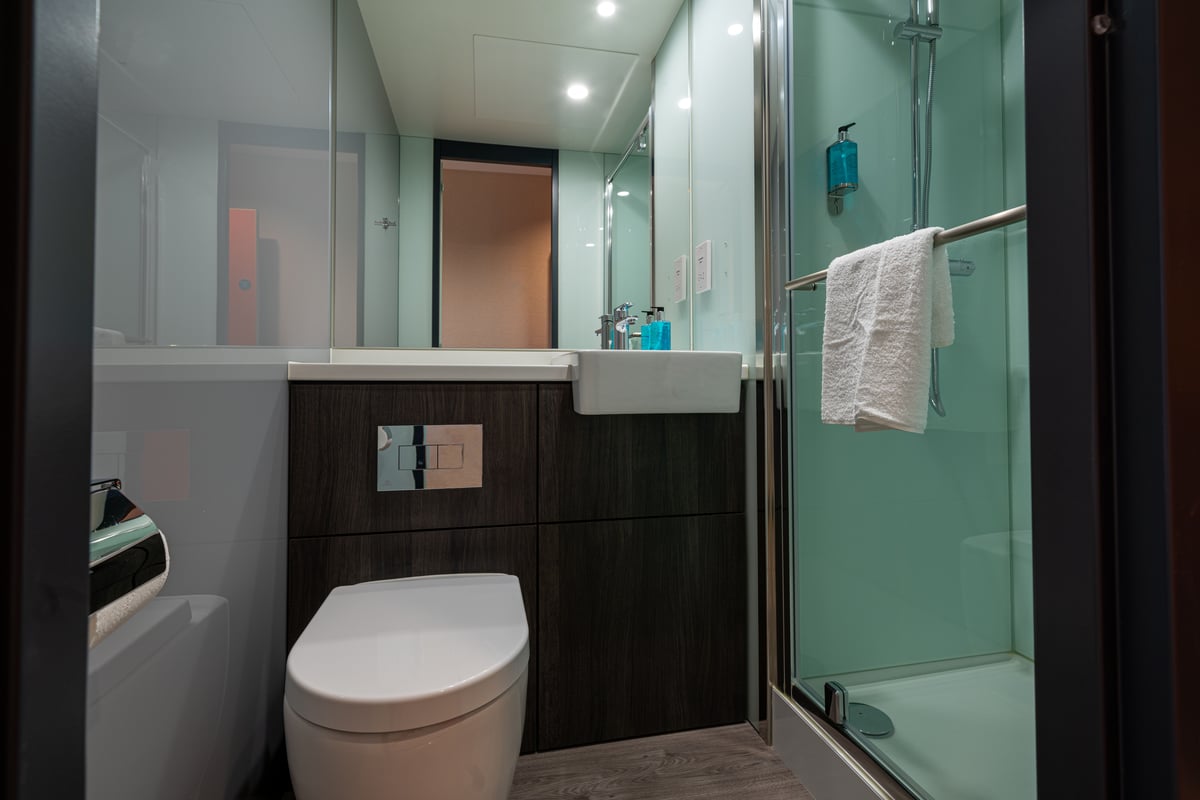 A small bathroom with a white toilet, a glass shower cubicle with a white bath towel and a toilet roll holder.