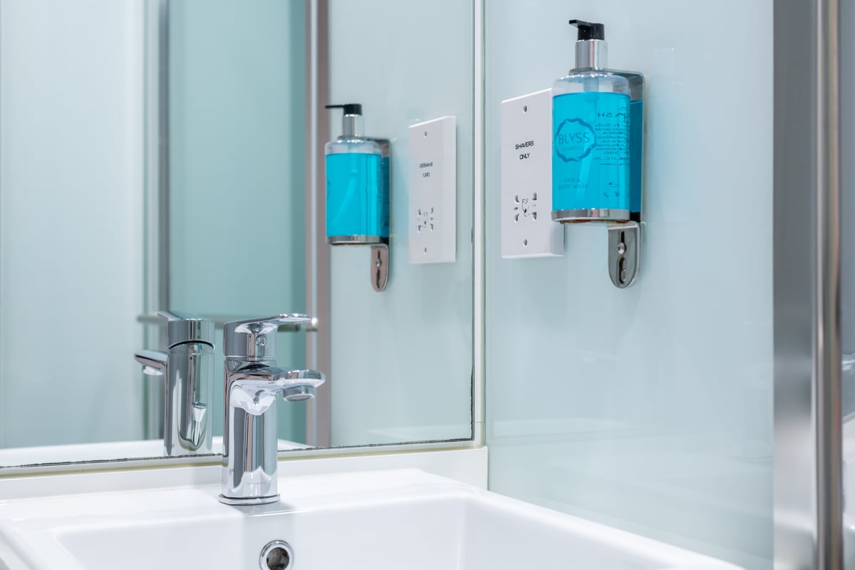 A modern easyHotel bathroom with a small sink, charging ports and hand wash mounted on the wall.
