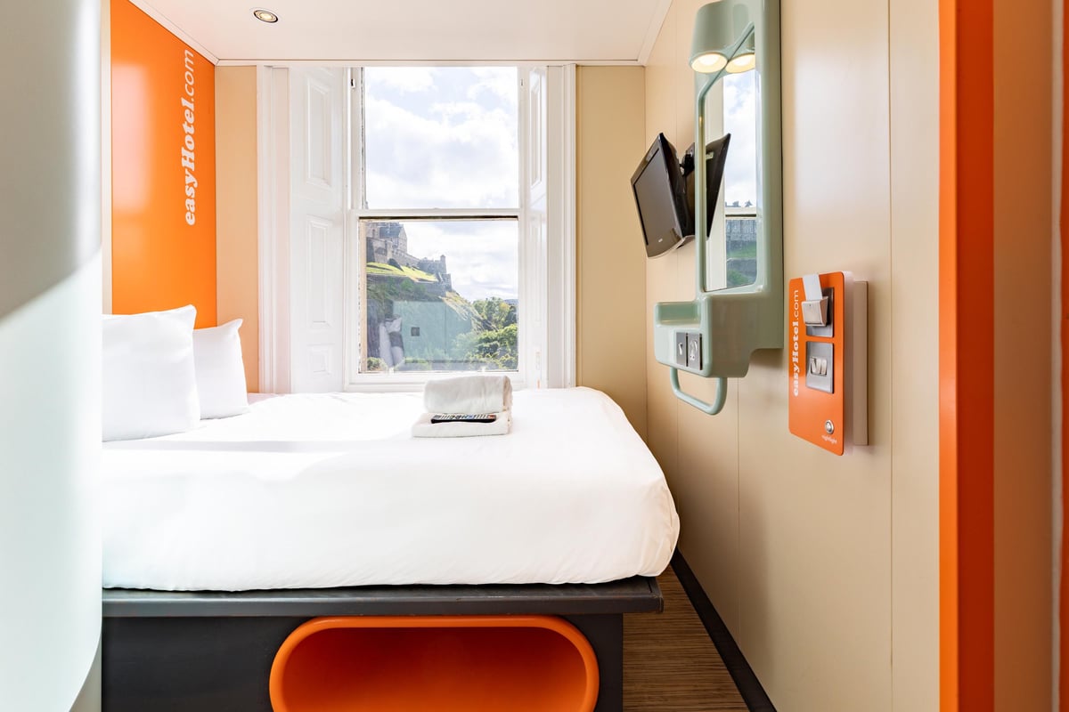 An easyHotel Edinburgh Double room featuring a comfortable bed, vibrant orange branding, and a window view of Edinburgh Castle.
