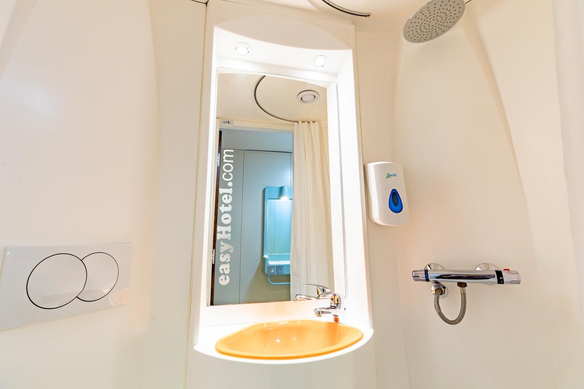 Compact easyHotel Edinburgh bathroom with an orange sink, mirror, shower, and toilet flush buttons.