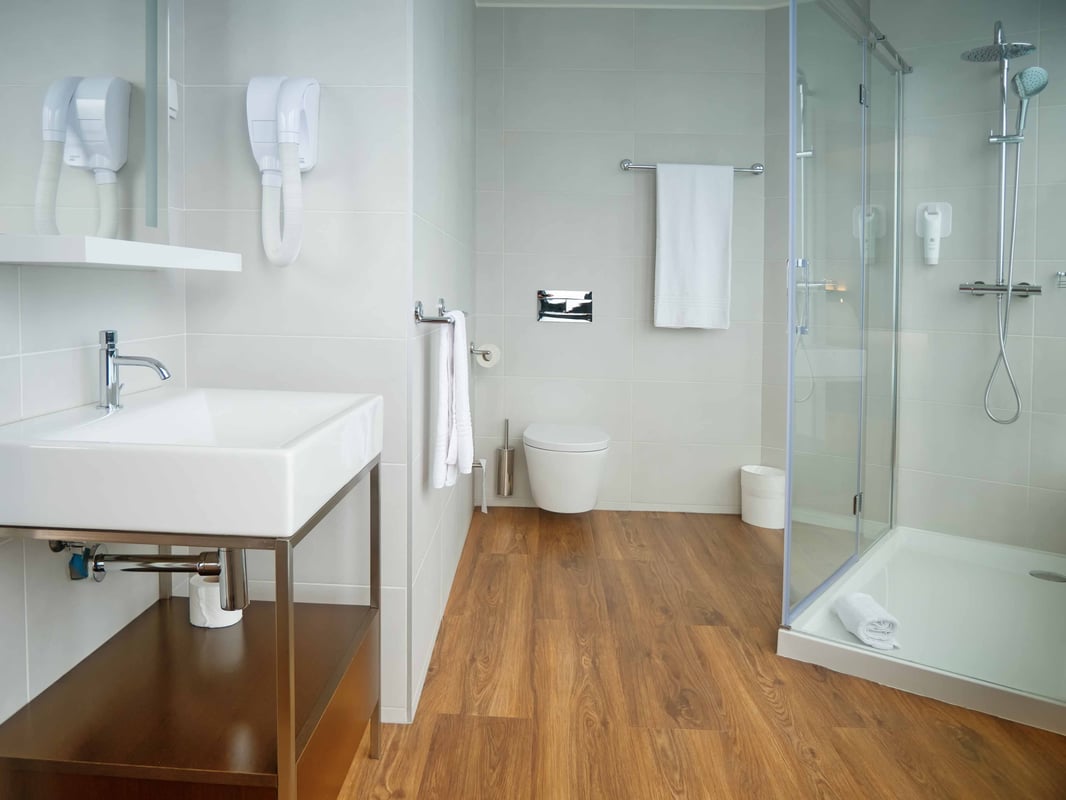 easyHotel Lisbon bathroom featuring a modern design with light grey tiled walls, wood-look flooring, a white sink, toilet, and a spacious glass-enclosed walk-in shower.