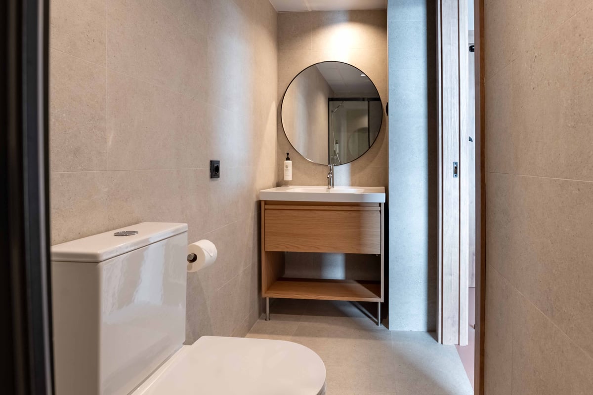 Modern easyHotel Madrid Alcalá bathroom with a toilet, wooden vanity, round mirror, and shower reflection.
