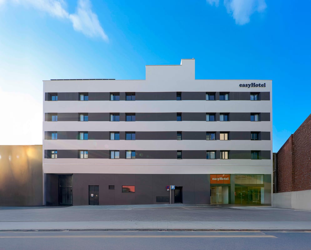 Exterior view of the modern easyHotel Madrid Alcala building, featuring a white and dark grey striped facade under a bright blue sky.