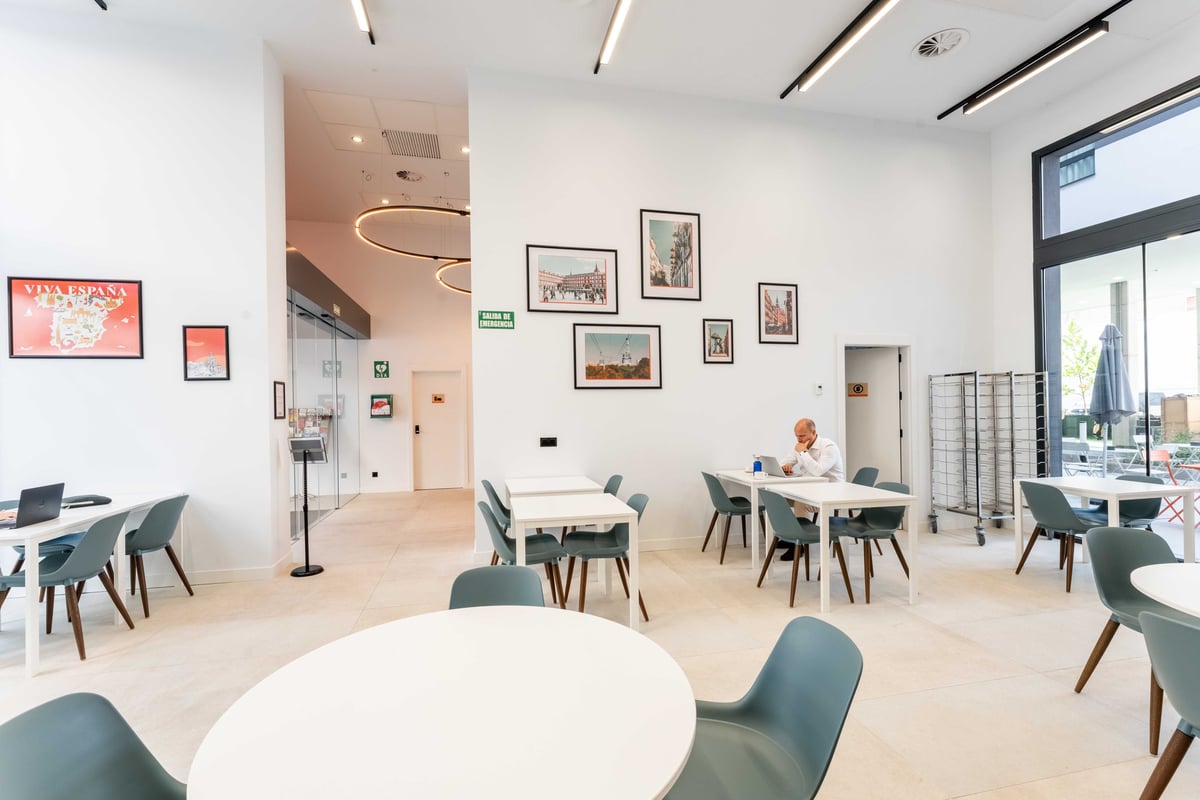 EasyHotel Madrid Alcalá restaurant dining area with white tables, blue chairs, and framed pictures on the white walls.