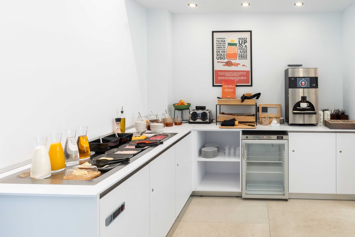 EasyHotel Madrid Alcalá restaurant breakfast buffet with coffee machine, juice dispensers, pastries, and various food options.
