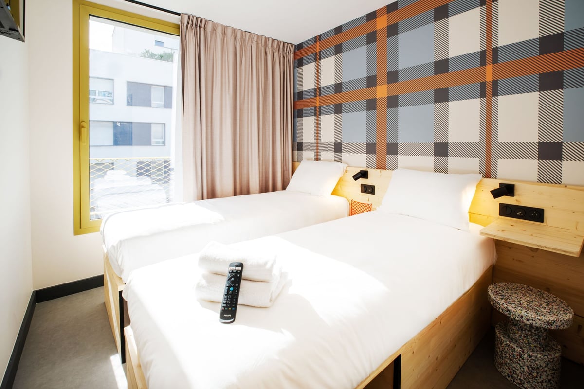 easyHotel Marseille twin room with two single beds, plaid accent wall, and a large window providing natural light.