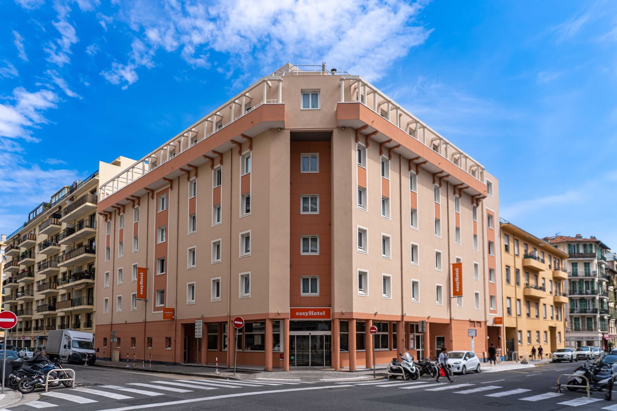 easyHotel Nice Old Town exterior, a multi-story budget hotel with a light beige and terracotta facade, located on a city street with crosswalks and parked scooters and cars.