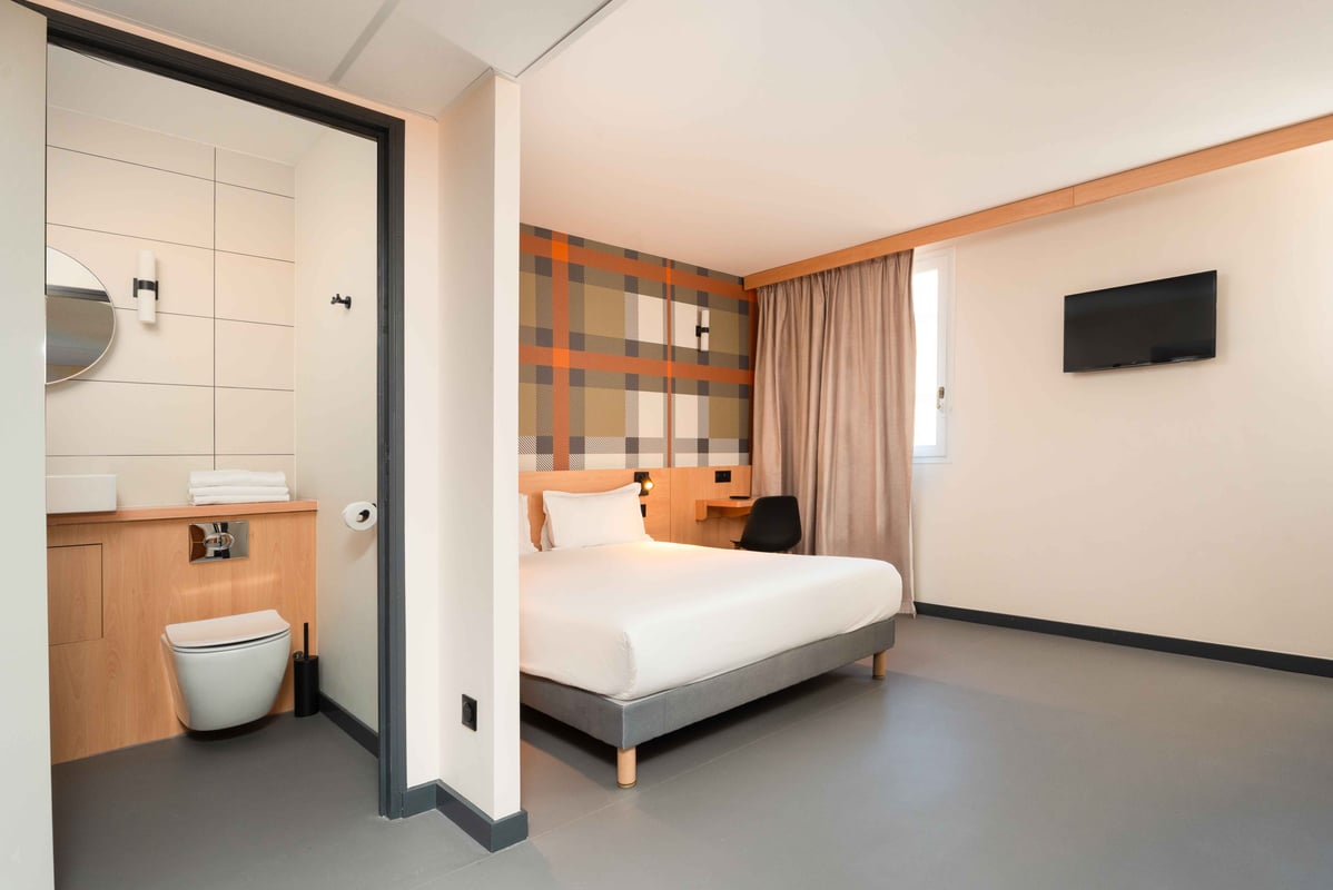 Modern easyHotel Nice Old Town room with a double bed, orange and brown plaid accent wall, desk, wall-mounted TV, and a visible en-suite bathroom area.
