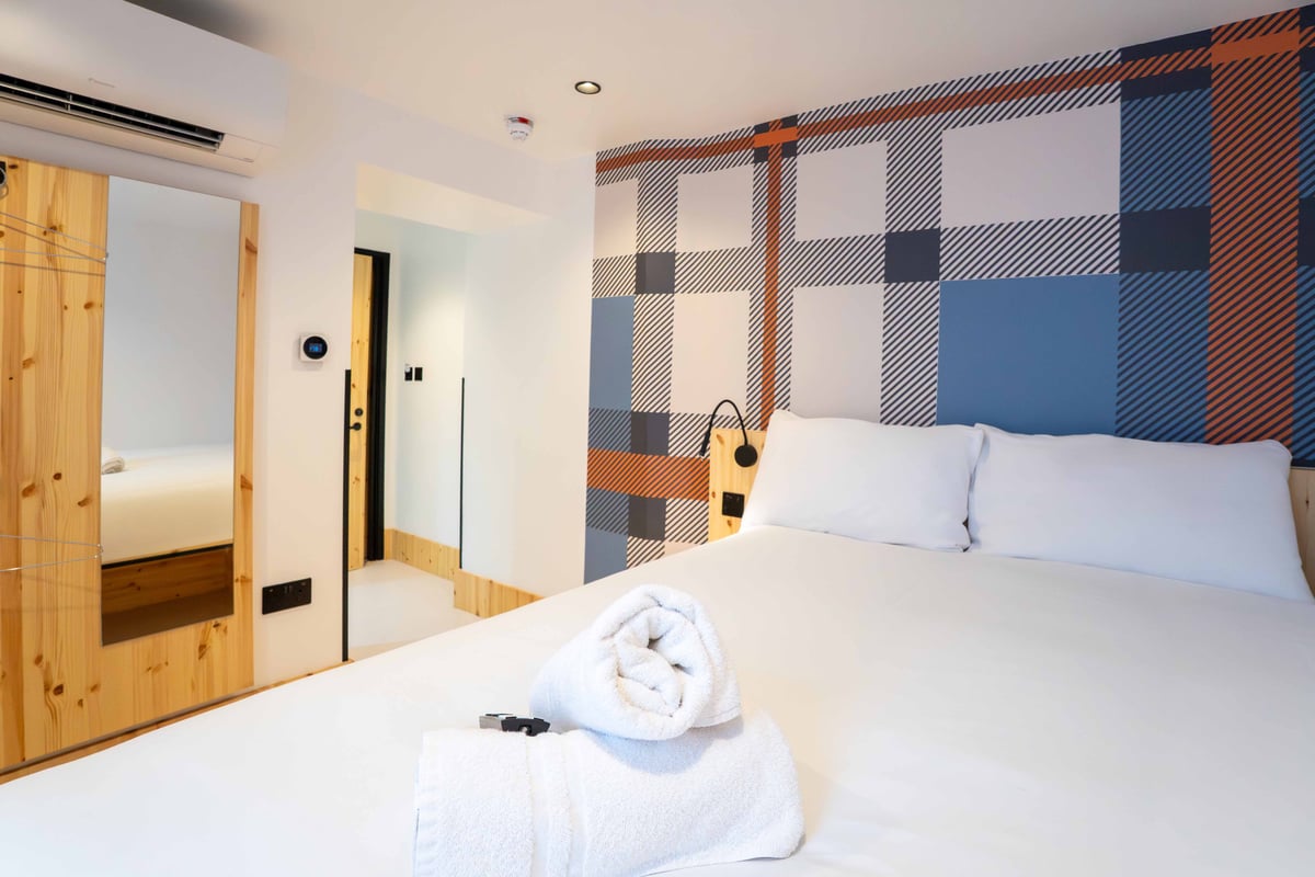 EasyHotel Paddington accessible double room with white linens, pillows, and a patterned headboard wall.